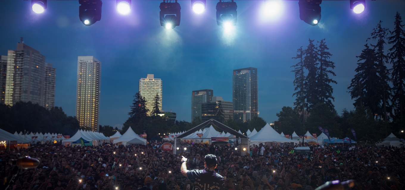 From the stage view of Sherry Mann performing to excited audience at Surrey Fusion Festival with city lights and night sky in background